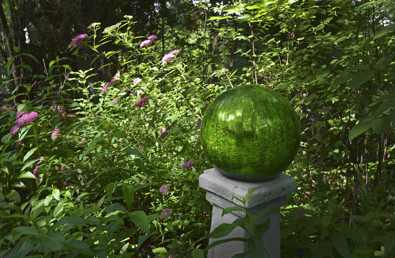 A magnificently green gazing ball sits atop a pedestal in an equally green garden.