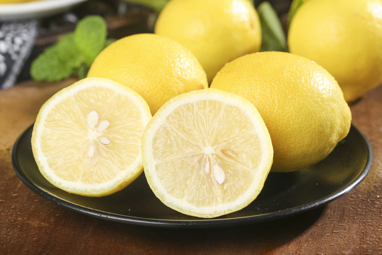 A few lemons on a plate with one split open to reveal its seeds.