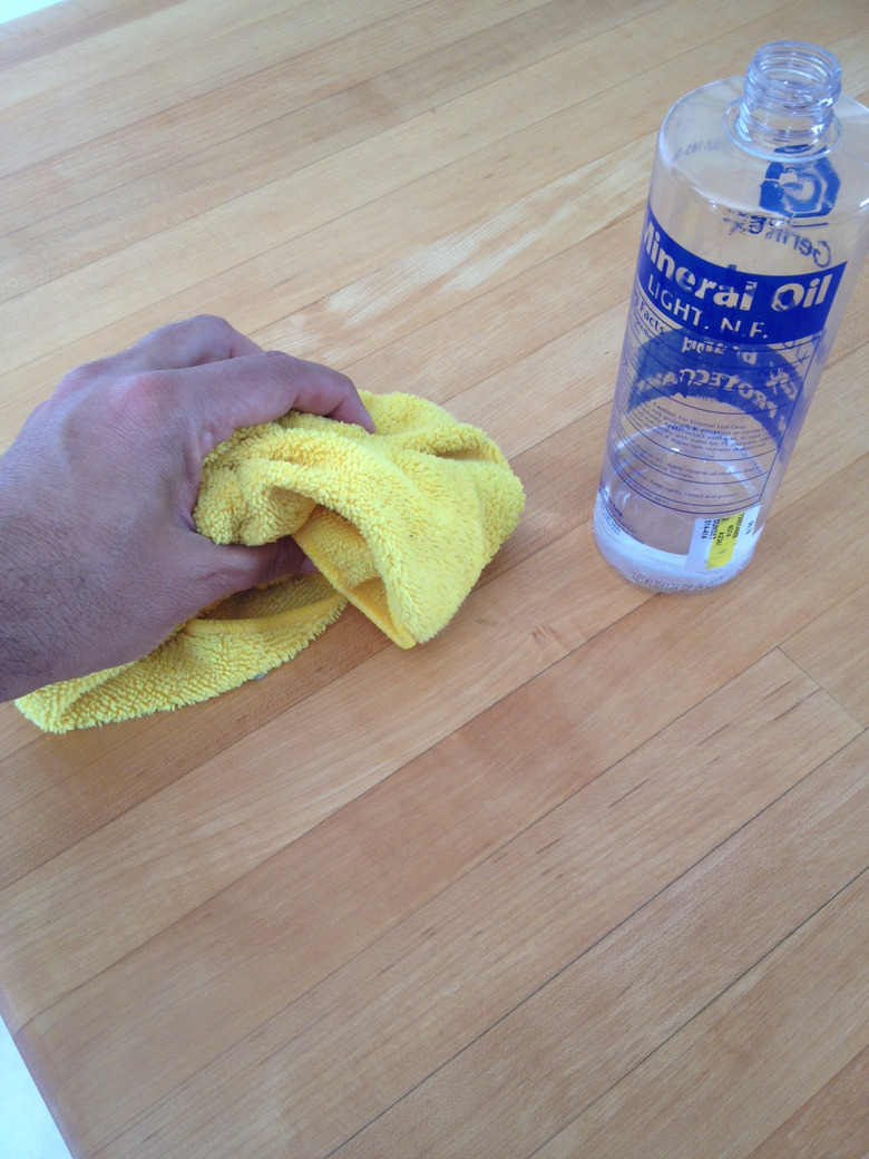 A hand using a rag to apply mineral oil to preserve a butcher block.