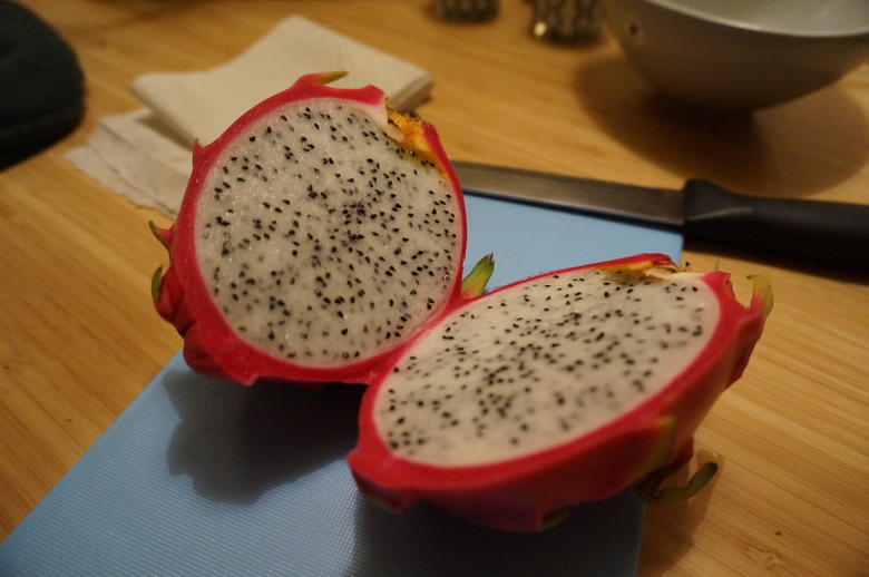 A red dragon fruit cut open on a countertop to reveal the white insides with black seeds.