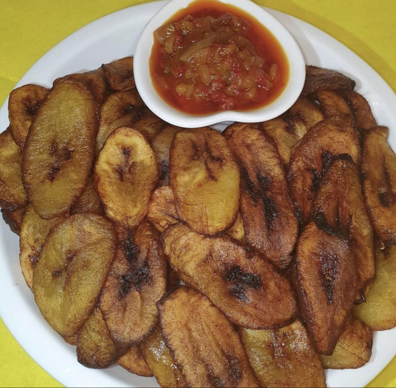Fried plantains on a white plate with a small cup of red sauce.