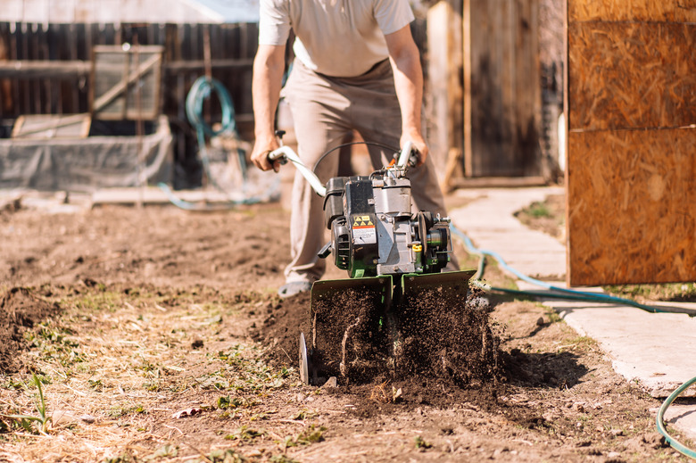A close-up photo of a gardener cultivating the ground soil with a rototiller.