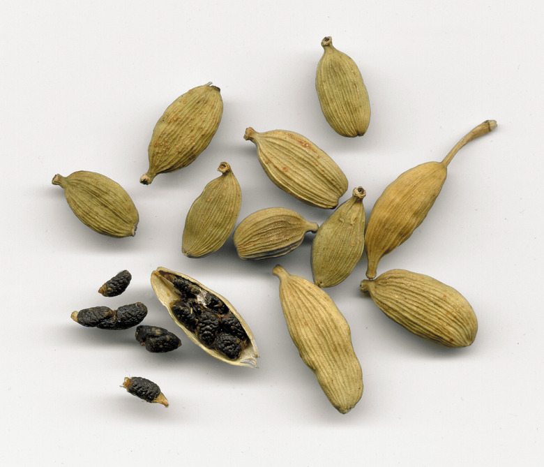 A handful of cardamom capsules with one broken open to reveal the seeds inside.