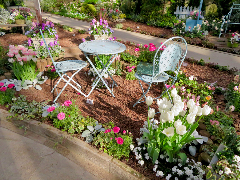 A raised bed with various flowers and some cute lawn furniture.