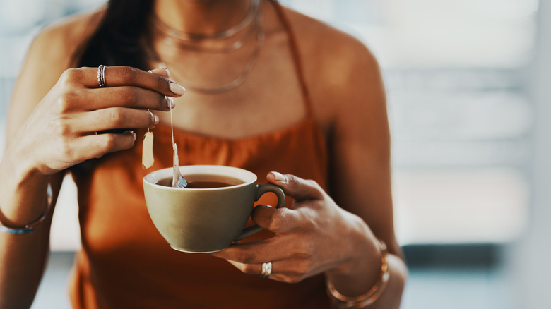 A woman dunks a tea bag into a hot cup of water.