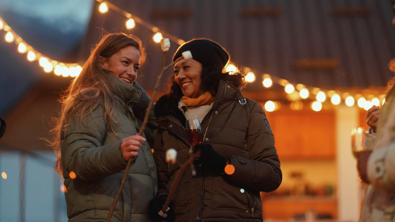Two women in winter jackets smile, as a strand of lights provides a cheery background.