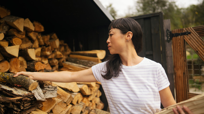 A woman grabs firewood from a stack.