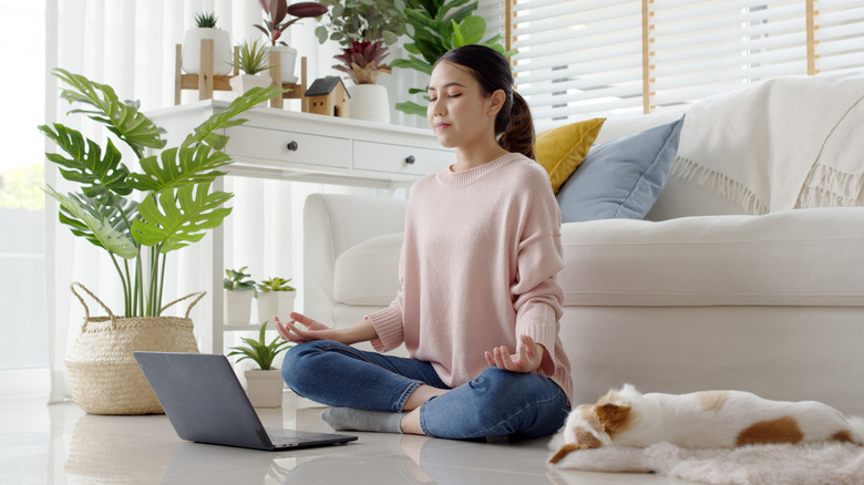 A woman meditates and breathes deeply near her house plant.
