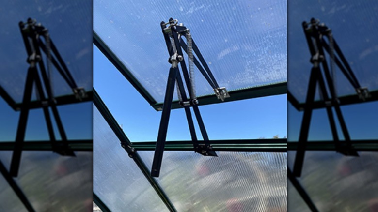 Image of the PATIOHZ greenhouse vent arms with the product in action against a blue sky.