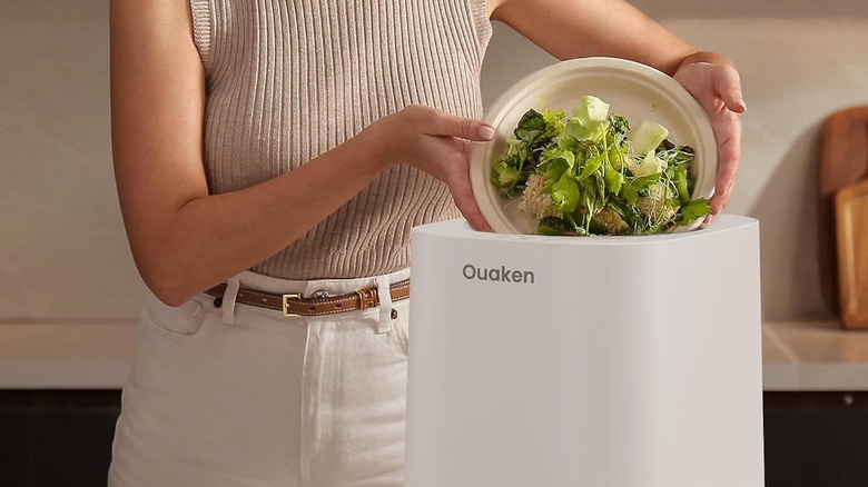 A woman in a beige sweater dumping a salad into a white Ouaken electric composter.