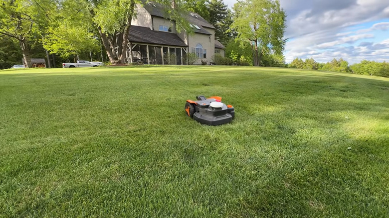 Orange and black WORX Landroid machine on a green lawn in front of a house on a cloudy day.