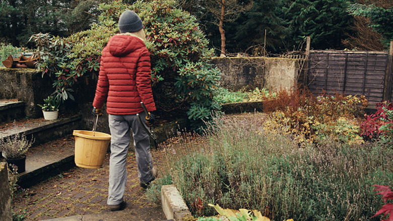A woman in a red jacket walking through a garden in fall holding tools