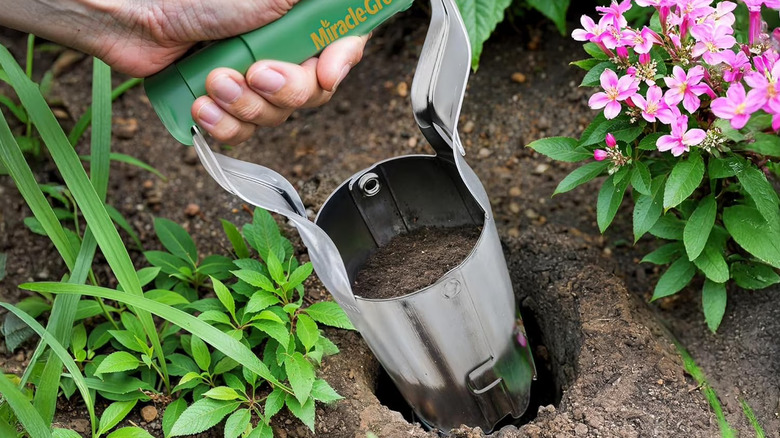 A gardener's hand using the green-handled Miracle-Gro bulb planter