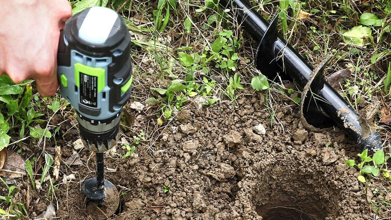 A hand using the WORKPRO Auger drill bit to drill a hole in the ground. Another black bit sits to the right