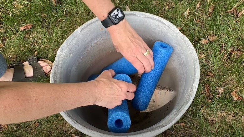 Woman puts pool noodles in the bottom of an empty garden planter.