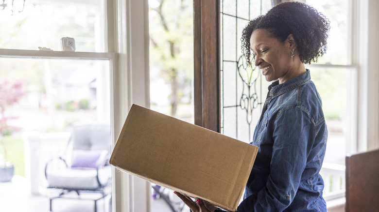 Woman holds a cardboard box at her front door.