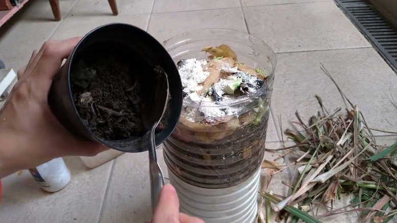 A person scoops dirt into a DIY compost bin.