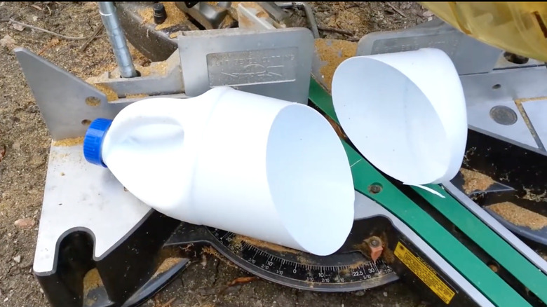 A plastic milk jug cut in half, placed on a workbench next to a saw and other DIY tools