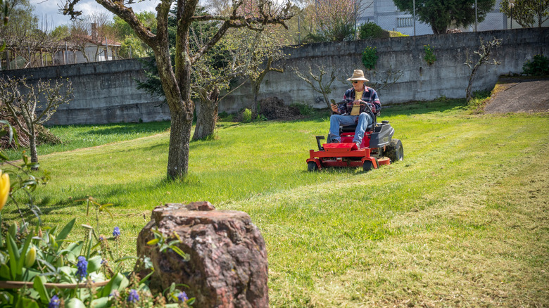 A man uses a riding mower to cut the grass in a large yard.