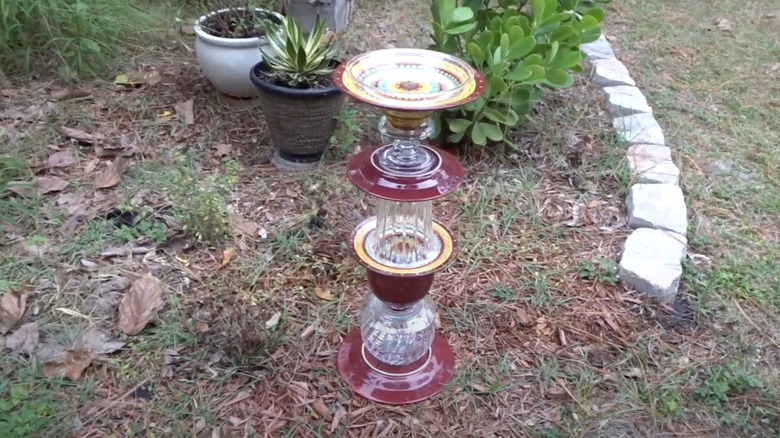 Saucers and glassware are stacked into a tower that is sitting outside in a garden.
