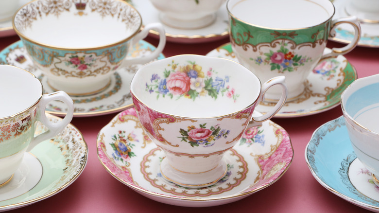 Sets of pastel floral tea cups and saucers are arranged on a pink surface.