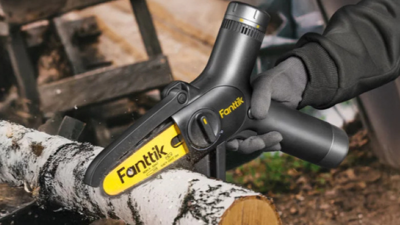 A black and yellow Fanttik handheld mini chainsaw being used to cut wood.