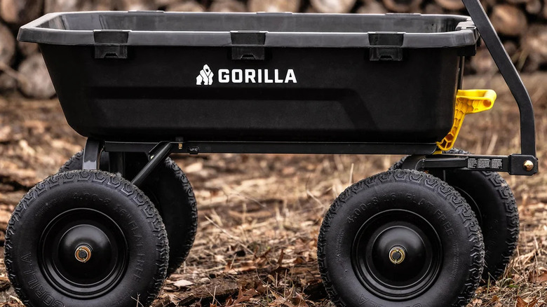 A black Gorilla dump cart with a yellow handle staged with dirt and logs