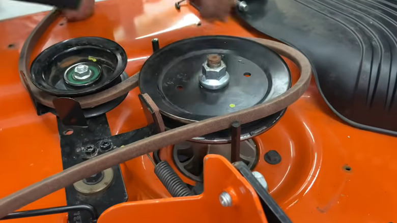 A mechanic works to replace a blade on a riding lawn mower.