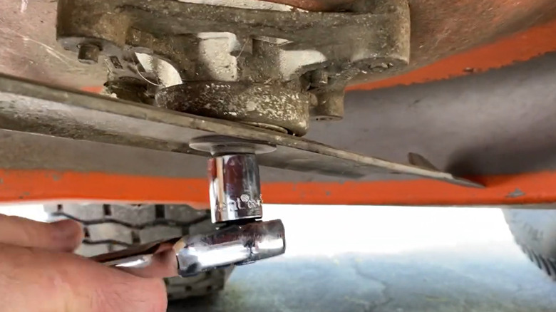 A homeowner removes the blade from their mower.