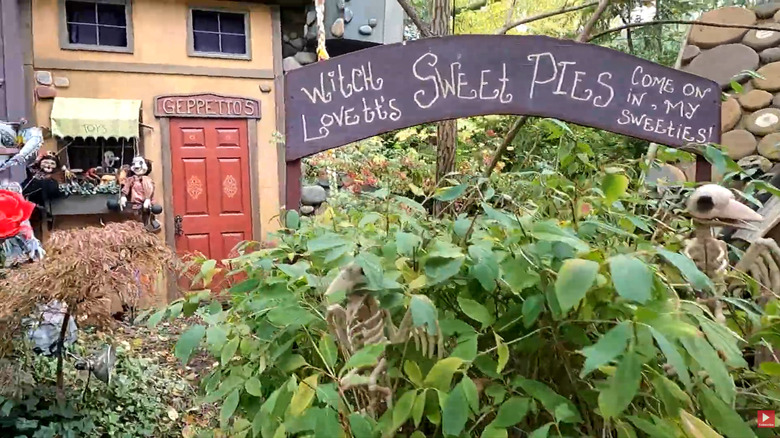 An elaborate garden display has fake buildings, skeletal decorations, and signs referencing famous fairy tales and films.