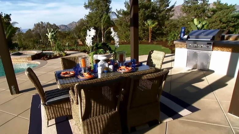 An outdoor kitchen and dining area are in the foreground and a pool is in the background.