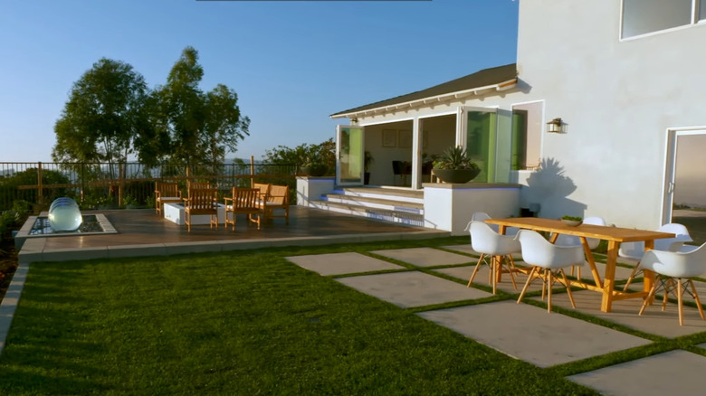 A backyard has multiple seating areas, a small spa, and an elegant lawn.