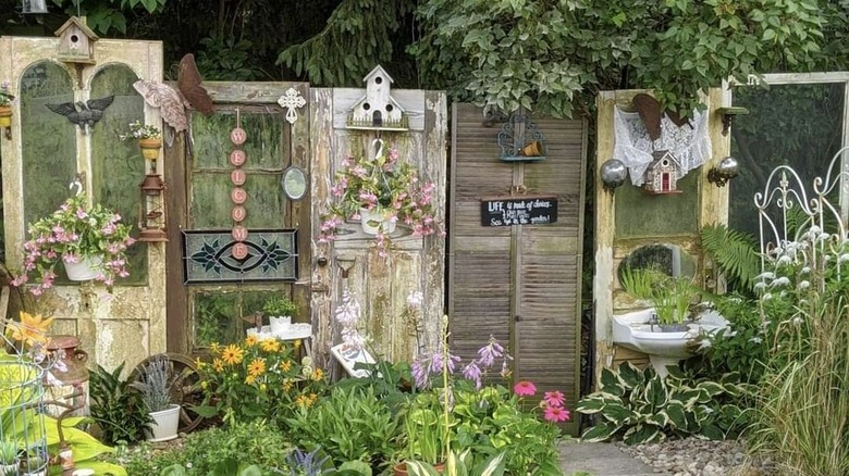 Vintage wooden doors, decorated with hanging planters and birdhouses, stand side by side as backyard decor.