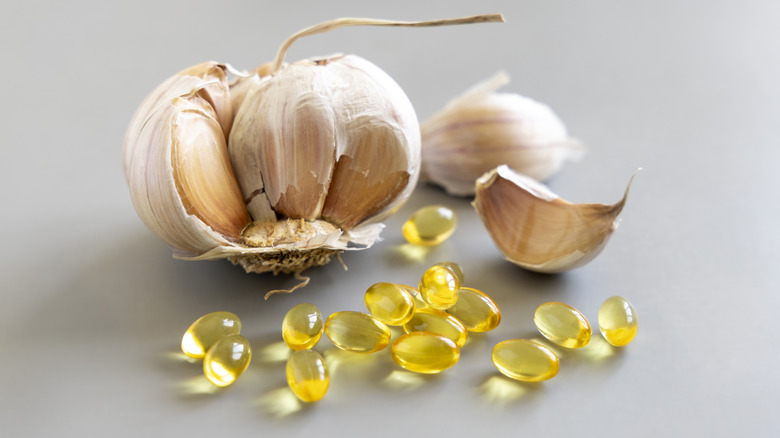 Garlic oil supplement pills sit near a garlic clove.