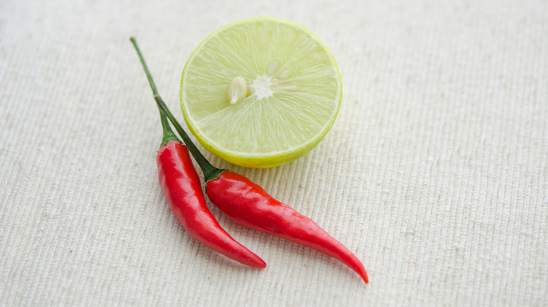 A sliced lime and red chili peppers lay on a cloth.