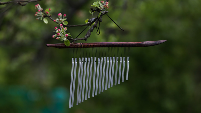 A wood and metal wind chime hangs from a flowering tree branch.
