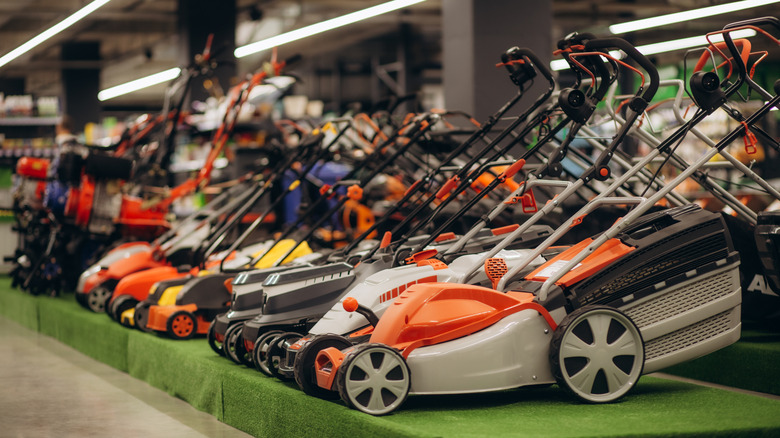 A row of colorful lawn mowers are lined up on display inside a well-lit hardware store.