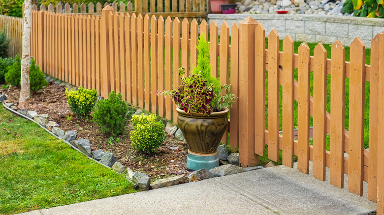 Shrubs and a potted plant lining a natural picket wooden fence.