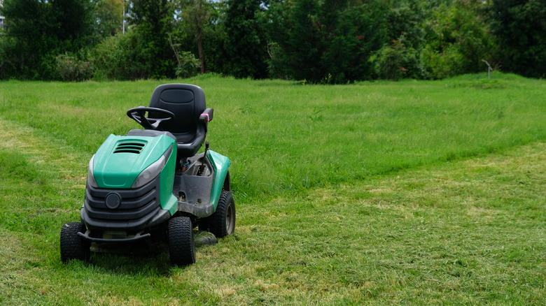 A green riding lawn mower sits on a half-mowed lawn.
