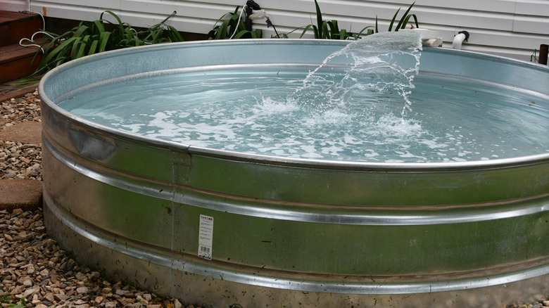 A small metal stock tank pool is in a backyard with water flowing into it.
