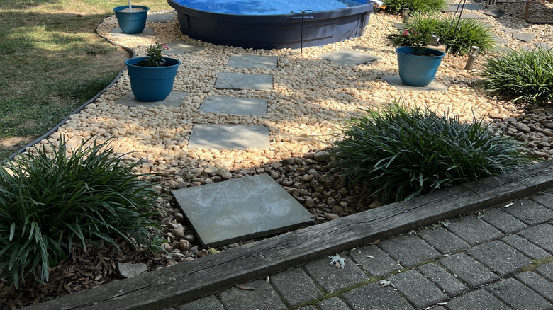 A stock tank pool is in a garden surrounded by plants and bird feeders.