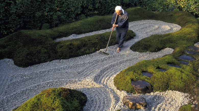 A person rakes gravel in a garden.