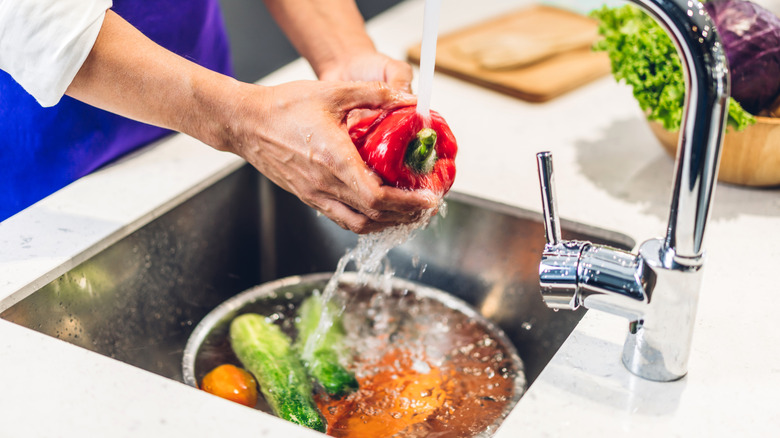 A cook washing fresh produce in a sink.