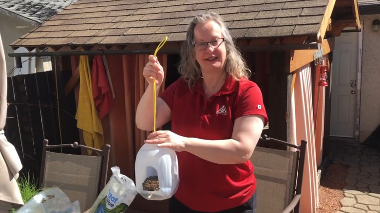 A woman holds a milk jug bird feeder she made.