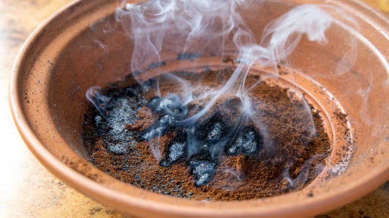 Smoke is rising from burnt coffee grounds in a clay bowl.