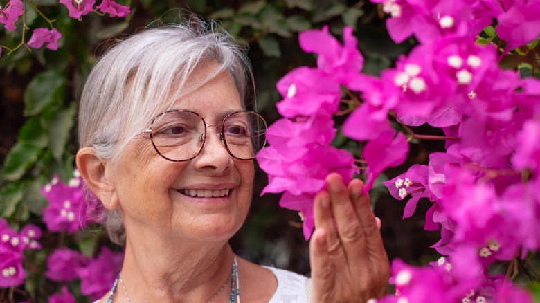 older woman wearing glasses looking at pink bougainvillea