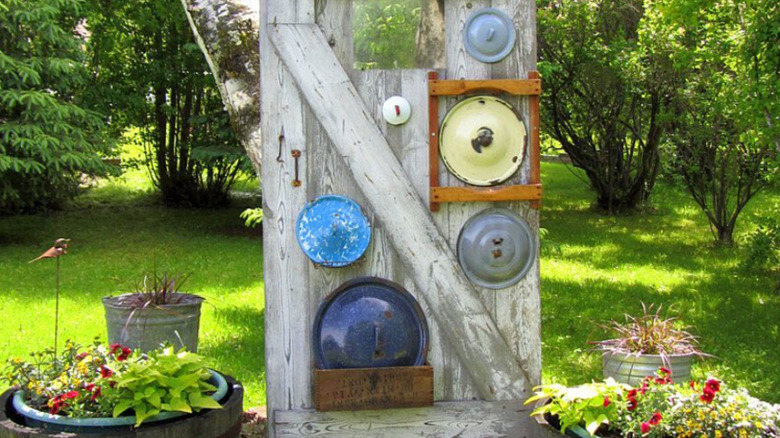 Colorful pot lids are attached to a door, creating unique garden decor.