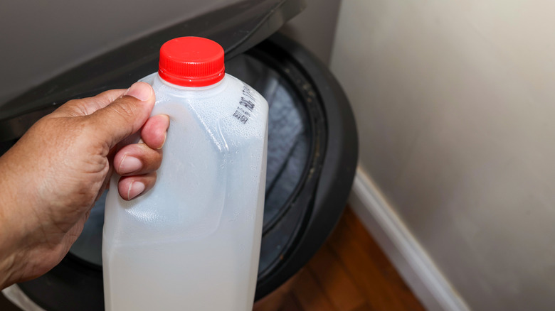A hand tosses an empty half-gallon of milk into an open trash can.