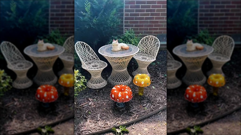 Two DIY mushroom statues are in front of some patio furniture in a garden bed.