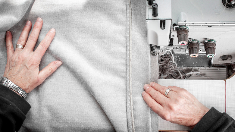 A pair of hands uses a sewing machine to sew a gray pillowcase.